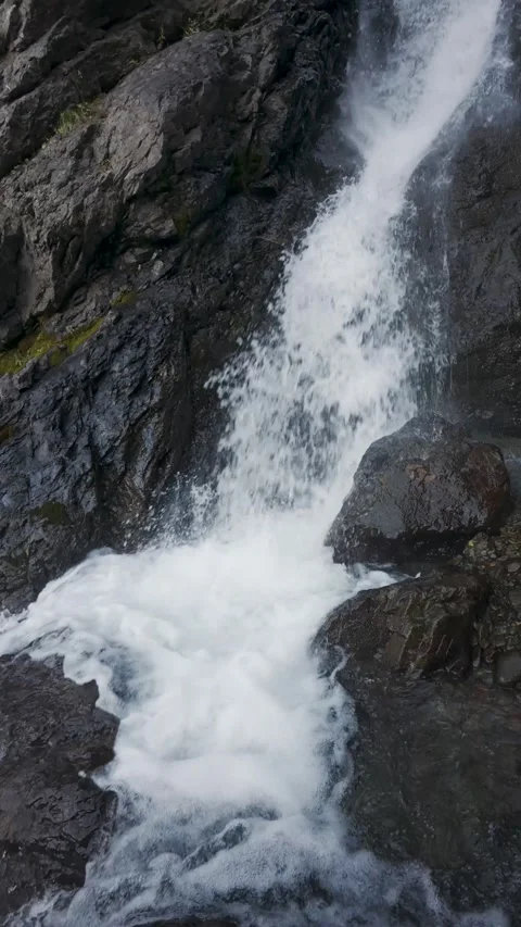 Vertical Slow Motion Tilt Up and Pan Reveal of Waterfall on Dark Rocks Stock Footage 330441075