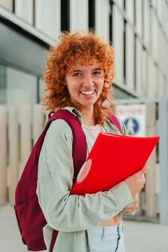 Vertical Smiling redhead student looking at camera while holding a red folder Stock Photos
