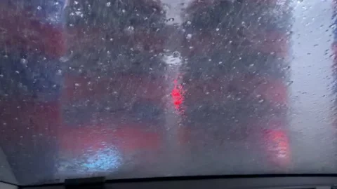 Vertical spinning brushes moving along sides of vehicle seen through wet windshi Stock Footage 330935587