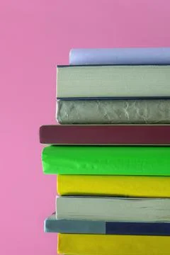 Vertical stack of colorful books against pink background. Copy space Stock Photos