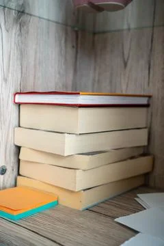 Vertical stack of worn books standing against a wooden panel wall in a cozy Stock Photos