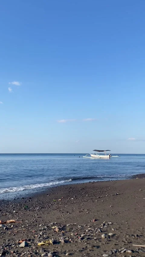 Vertical Static Shot of Boat Anchored on Bali Black Sand Beach Stock Footage 340411379