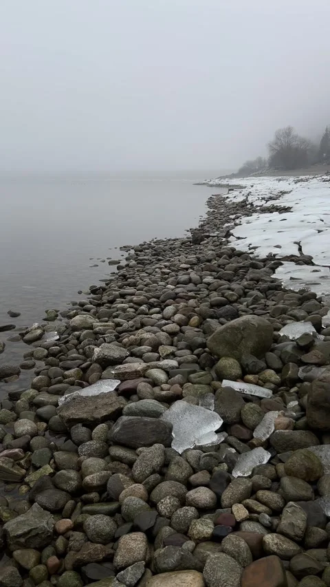 Vertical Static Shot of Icy Rocky Lake Shore with Morning Fog and Mist Stock Footage 328473780