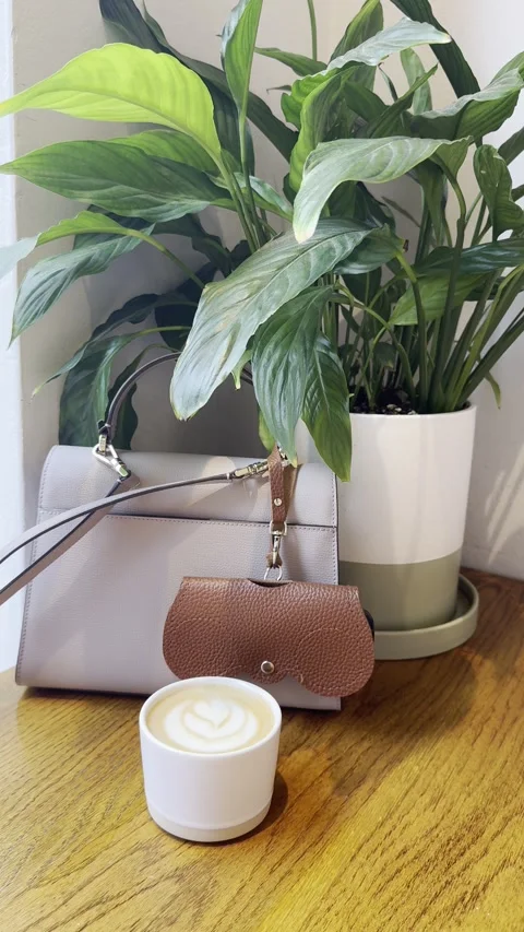 Vertical static shot of luxury handbag coffee cup and green plant on cafe table Stock Footage 336680153