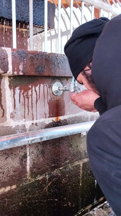 Vertical static shot of a man cupping his hands to drink or collect water from a Vídeos de archivo 334660134
