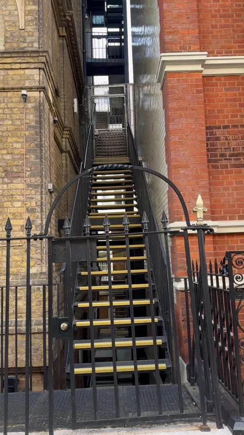 Vertical static shot of metal fire escape stairs between London buildings Stock Footage 337324194