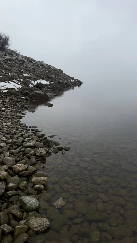 Vertical Static Shot of Rocky Lake Shore with Ice Sheets and Thick Morning Fog Stock Footage 328473771