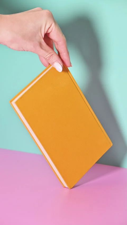 Vertical Stop Motion of Hand-Held Rotating Yellow Book on Pastel Background Stock Footage 258598015