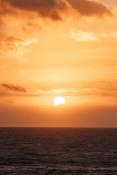 Vertical sunset over the ocean creates a vibrant orange sky and calm waters Stock Photos