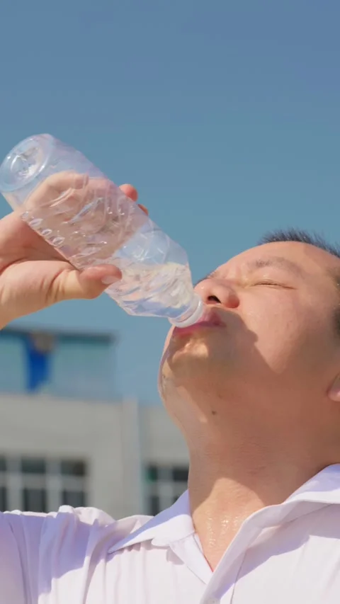 Vertical sweating profusely in the heat, man gulps down a whole bottle of water Vídeo Stock 336037511