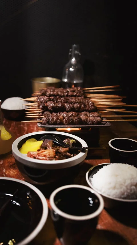 Vertical table spread with grilled meat skewers rice kimchi and drinks Stock Footage 333878782