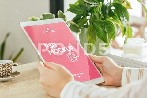 Vertical tablet mockup held by a woman who is in the living room PSD Template