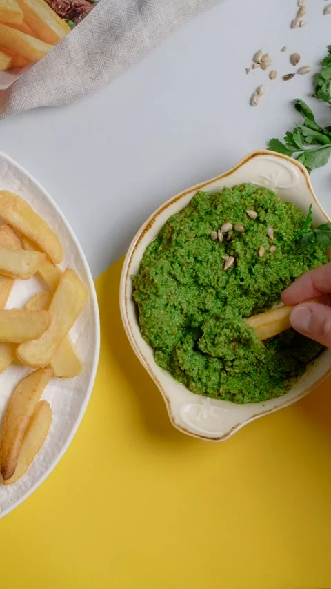 Vertical tabletop video: man scoops up pesto sauce with crispy potato wedges Stock Footage 178917185