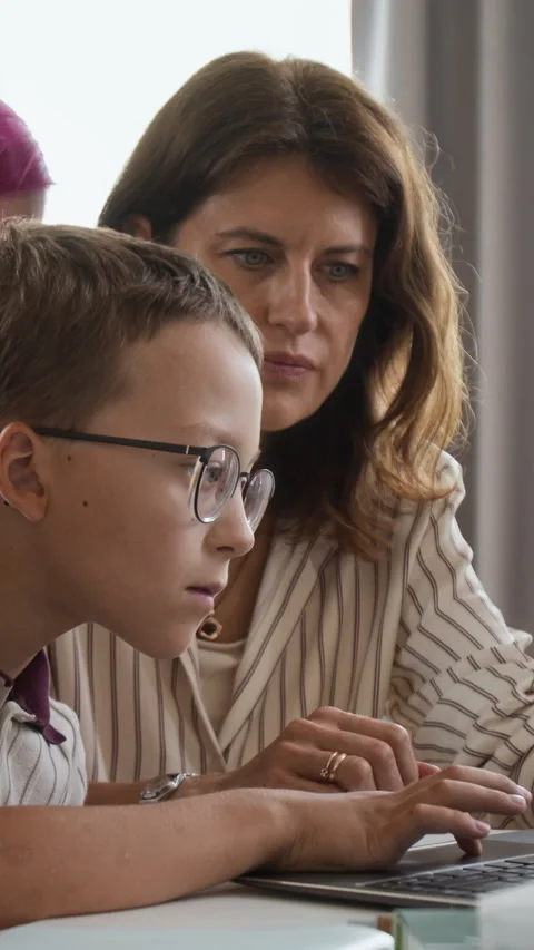 Vertical of Teacher Assisting Schoolboy Using Laptop Computer in Classroom Stock Footage 345226913
