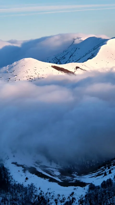 Vertical timelapse of clouds flowing like waterfall over snowy winter mountain 動画素材 321751555