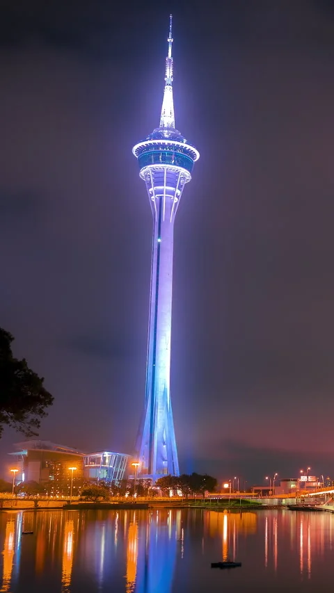 Vertical timelapse of Macau Tower glowing above the waterfront at night Stock Footage 344371873