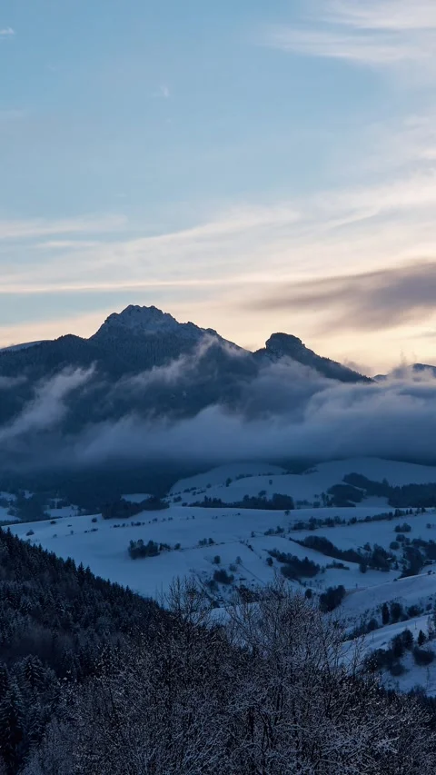 Vertical timelapse of misty clouds rolling over winter mountain peaks during a 스톡 동영상 336394319