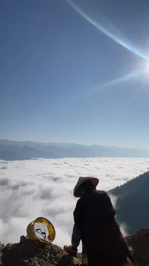 Vertical timelapse of person wearing conical hat sitting on mountain peak ov Video stock 327690071