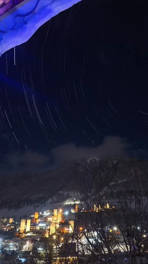 Vertical timelapse star trails spinning over illuminated mountain village M.. Video stock 341415154