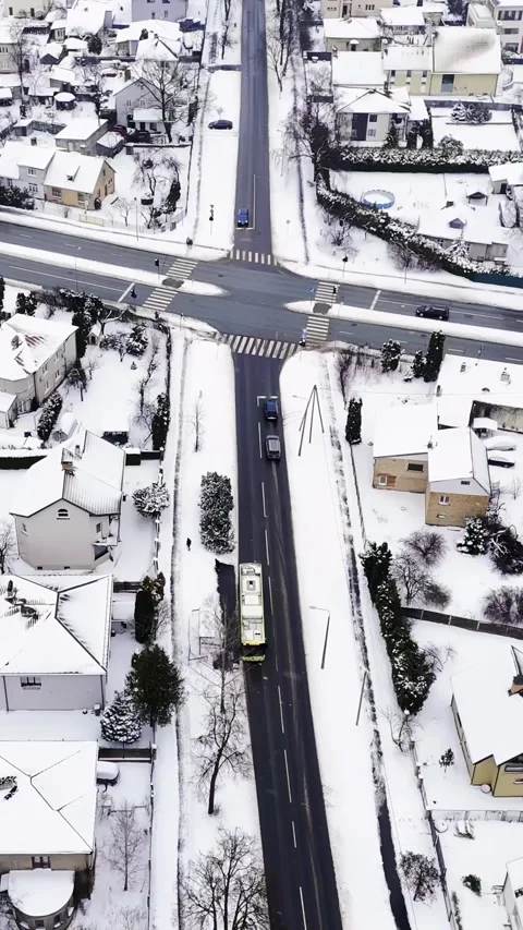Vertical top-down drone shot of a city bus and cars crossing a snowy suburban Stock Footage 328635979