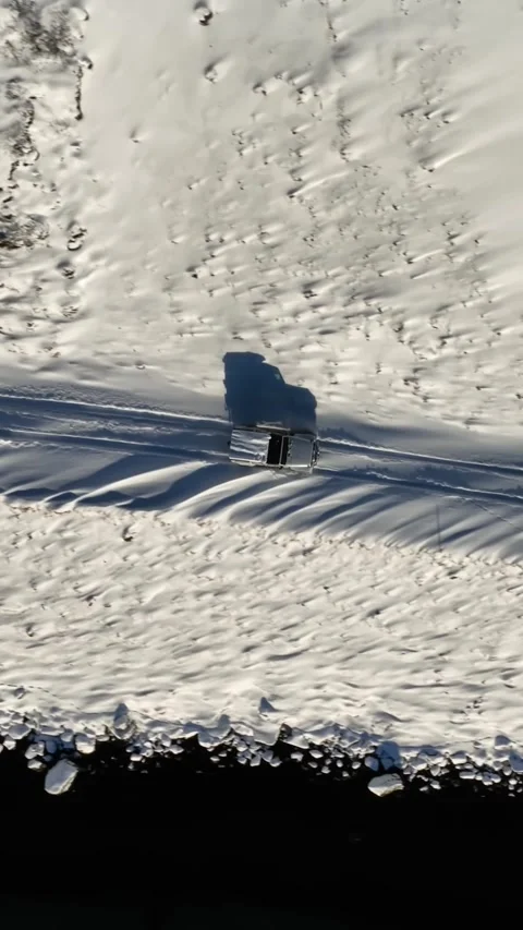Vertical top-down drone view of a lone 4x4 driving along the snowy shoreline of Vídeo Stock 334581167