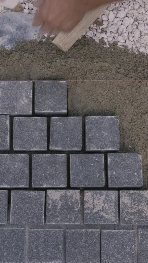 Vertical top down view of a builder installing gray paving stones with a mallet Stock Footage 345412339
