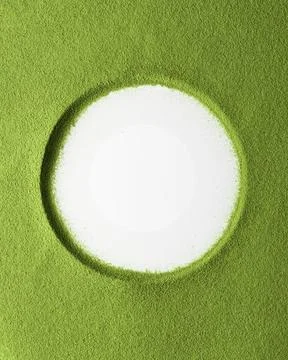 Vertical top down view of a white circle resting in bright matcha powder that Stock Photos
