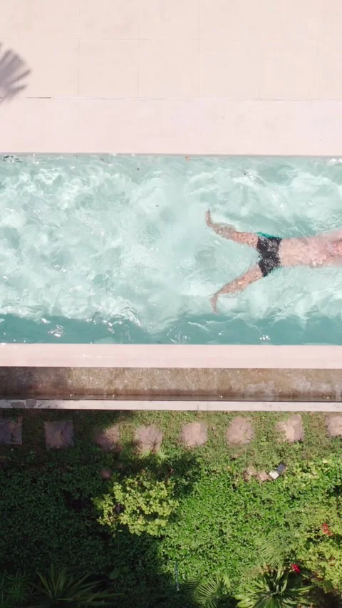 Vertical top Drone shot of a Man Enjoying a Swim in a Pool on sunny day Stock Footage 279471116