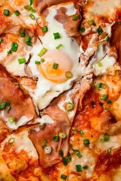 Vertical top view on appetizing hot pizza with prosciutto, egg and green onion Stock Photos