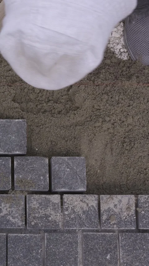 Vertical top view of a builder laying gray paving stones on sand Stock Footage 345412272