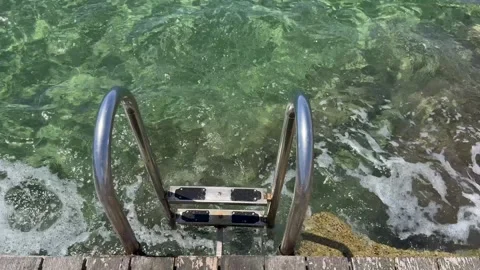 Vertical tracking shot looking down a metal ladder into wavy crystal clear sea Stock Footage 336320425