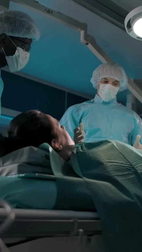Vertical of Two colleagues in the operating room move a couch with a female Stock Footage 276928384