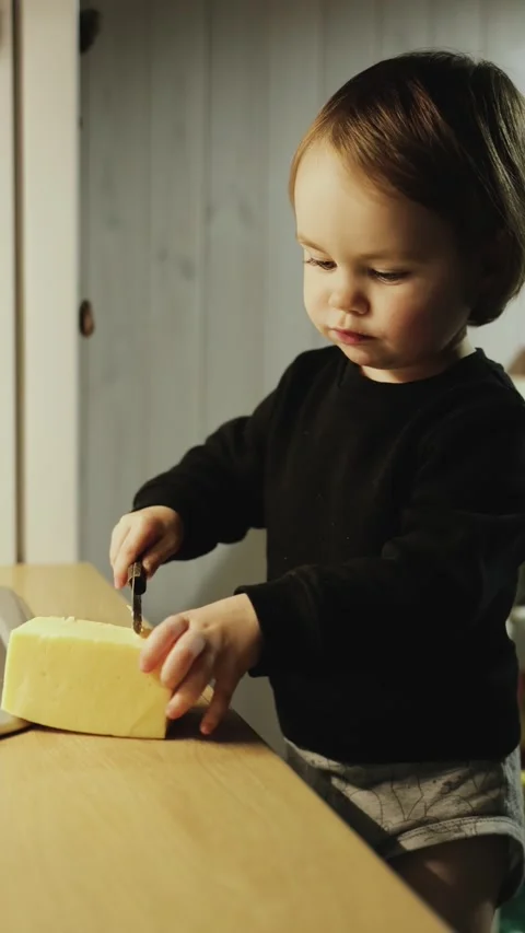 Vertical video. 3 year old girl cutting cheese with a knife in a cozy kitchen Stock Footage 321944578