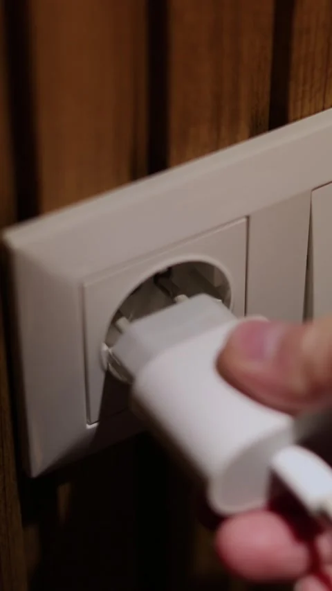 Vertical video. 60 fps. Man inserts charger plug of gadget in white wall socket Stock Footage 326825631
