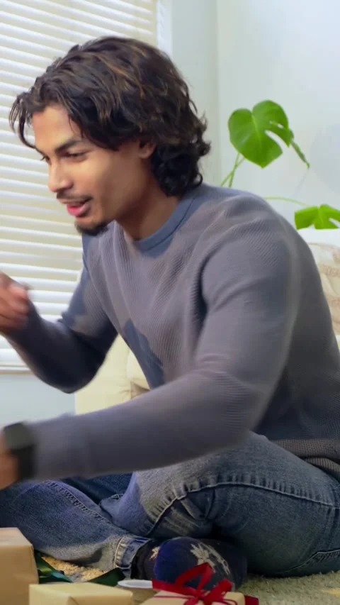 Vertical video: Accepting gift from partner, man in sweater at home checking hat Stock Footage 348273860