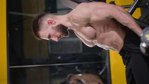 Vertical video. Active athlete training biceps by lifting dumbbells in a dark Stock-Footage 264760545
