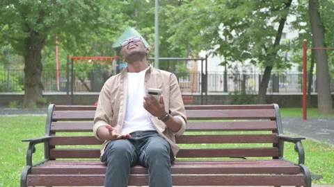 Vertical Video, African Man Facing Loss on Smartphone, Sitting Outdoor on Bench Stock Footage 310833494