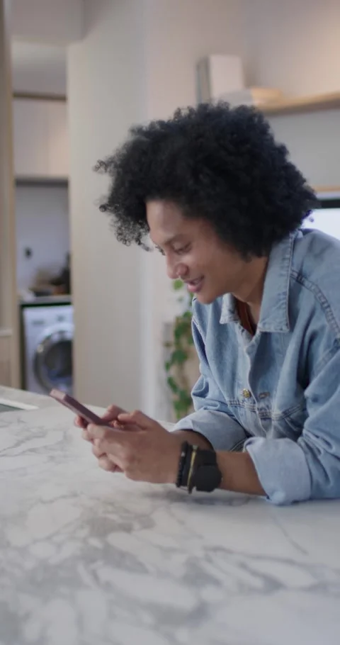 Vertical video: African man leaning on marble counter in kitchen, scrolling Stock Footage 337260146