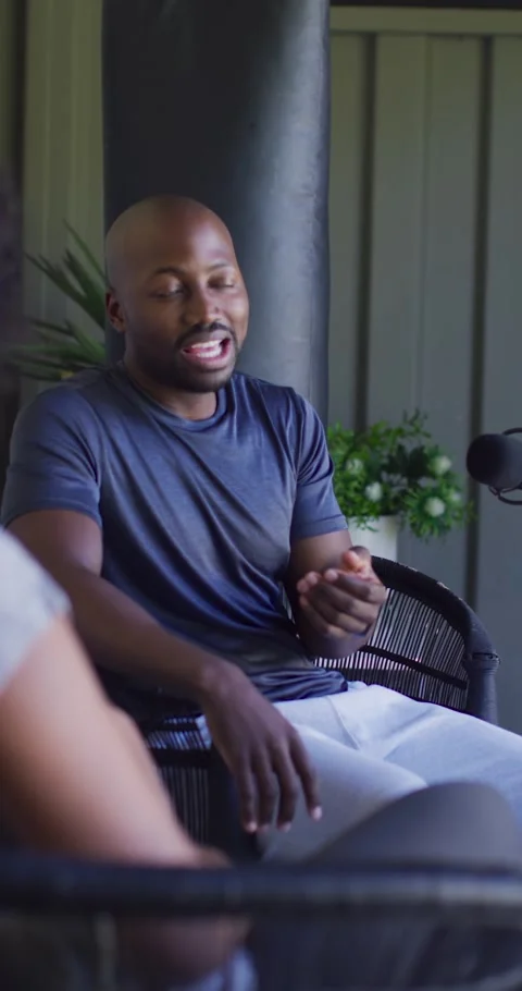 Vertical video: African man in navy tee responding to partner question on porch, Stock Footage 345493524