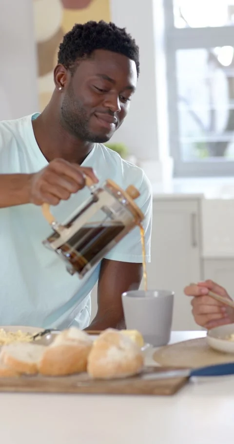 Vertical video: African man pouring French press coffee into grey mug in kitchen Stock Footage 345040922