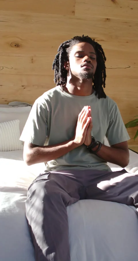 Vertical video: African man praying on bed, meditating as sunlight brightening, Stock Footage 345220099