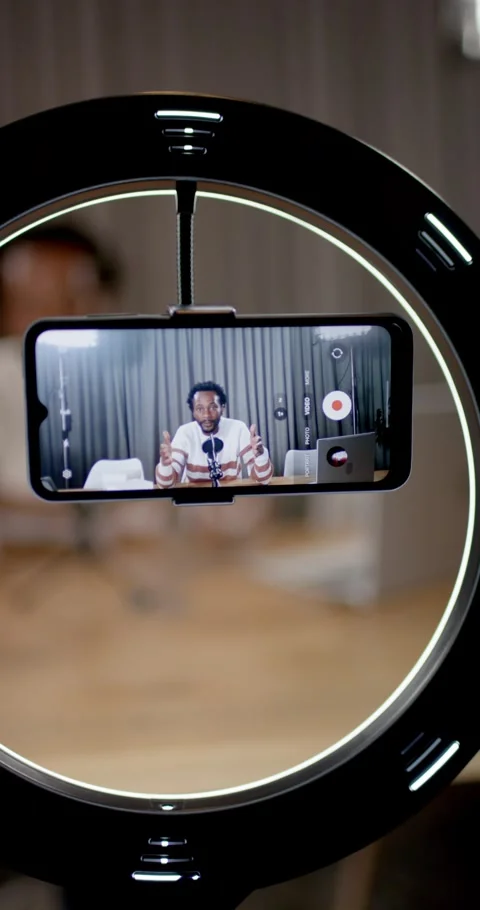 Vertical video: African man recording with mic at desk, ring framing phone Stock Footage 345591891