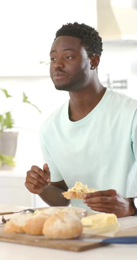 Vertical video: African man sitting at kitchen counter hungry, sampling bowl, Stock Footage 345397447