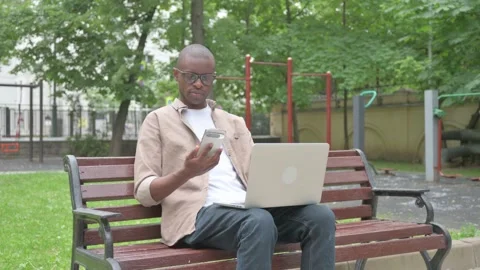 Vertical Video, African Man Using Smartphone and Laptop while Sitting Outdoor 스톡 동영상 310833928