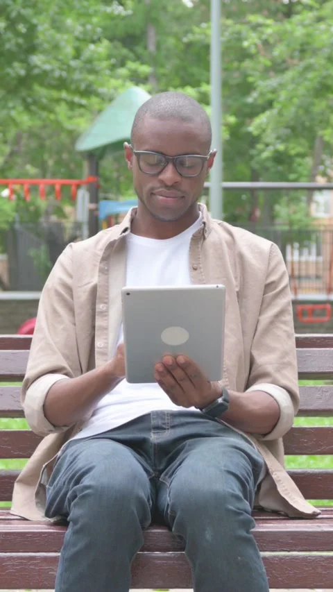 Vertical Video, African Man Using a Digital Tablet Outdoor on Bench Stock Footage 318042200