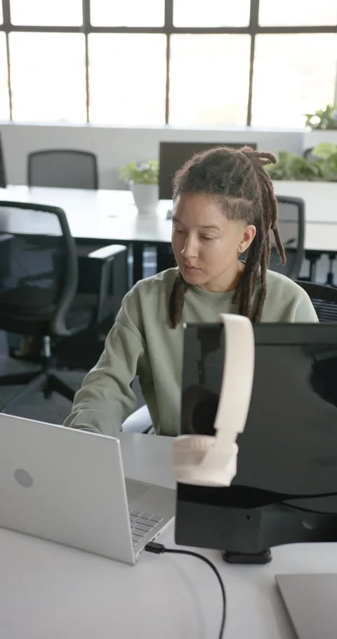 Vertical video: African nonbinary worker looking at laptop typing tapping tablet Stock Footage 344695578