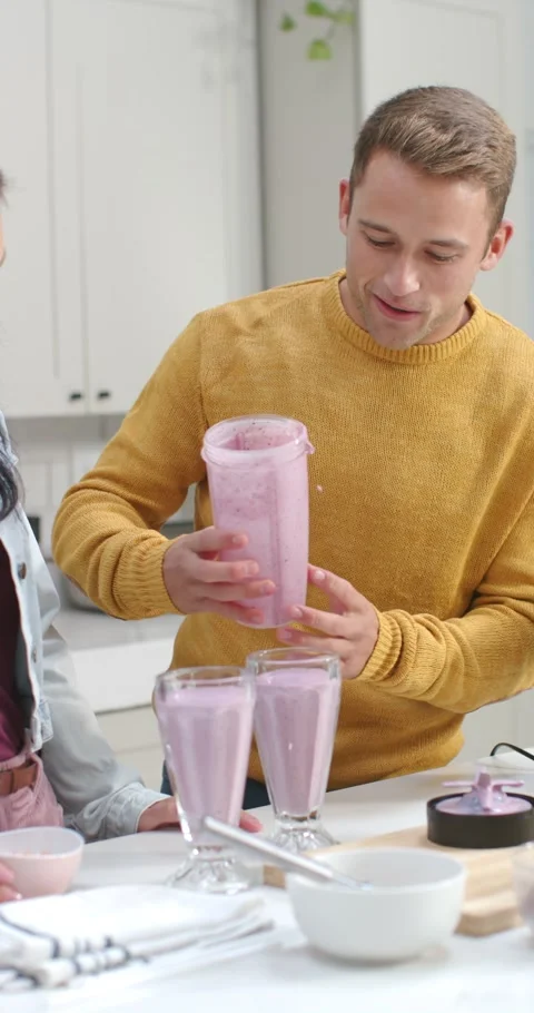 Vertical video: After blending Couple pouring from blender cup into 2 cups at Video stock 344695166