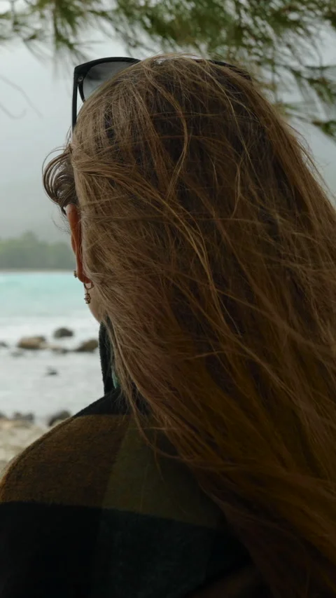 Vertical video. Alone on an empty seaside in a cool day, a woman shelters under Stock Footage 262283095