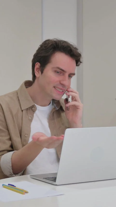 Vertical Video, Angry Young Creative Man Talking on Phone While Working on Video stock 318045168