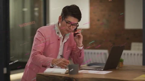 Vertical video: Answering phone call, Asian man in pink blazer writing notes at Stock Footage 334120499